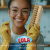 Smiling woman in yellow gloves holding Lola coco bristle hand scrub brush in kitchen, American owned and operated since 1969