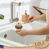 Hand using Lola dishwashing brush to scrub a white plate at sink; American owned family business since 1969