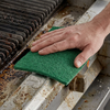 Green LOLA Pot Brite scouring pad scrubbing residue from a barbecue grate.