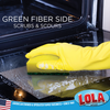 Green fiber side of scrub sponge scrubs and scours oven surface with yellow-gloved hand for kitchen cleaning