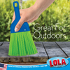 Hand holding green bristle whisk broom sweeping weathered wood deck boards outdoors with garden in background
